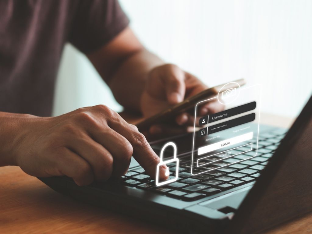 Una persona frente al computador sostiene un celular en una mano, y con la otra simula en el aire comprar un certificado digital por internet.